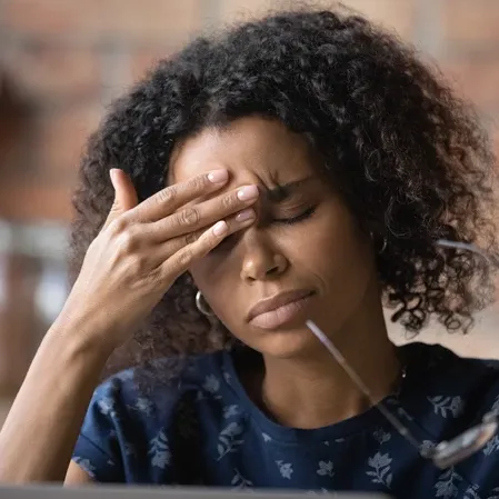 A woman removing her glasses to massage her forehead, with a headache