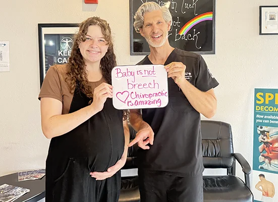 Pregnant patient with chiropractor holding a sign that reads, “Baby is not breech. Chiropractic is amazing.”
