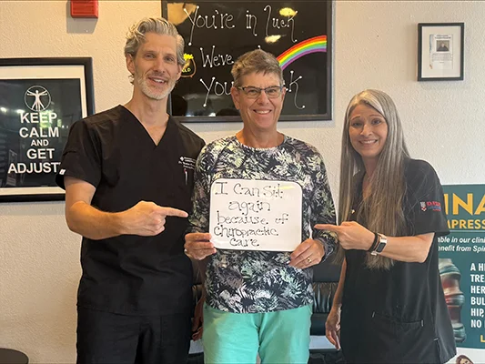 Patient with chiropractic staff holding a sign that reads, “I can sit again because of chiropractic care.”