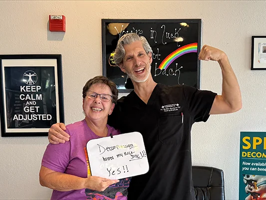 Patient with chiropractor holding a sign that reads, “Decompression helped my muscle disc!!! Yes!!”