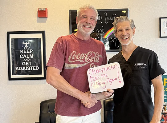 Patient shaking hands with chiropractor while holding a sign that reads, “Chiropractic has me golfing again.”