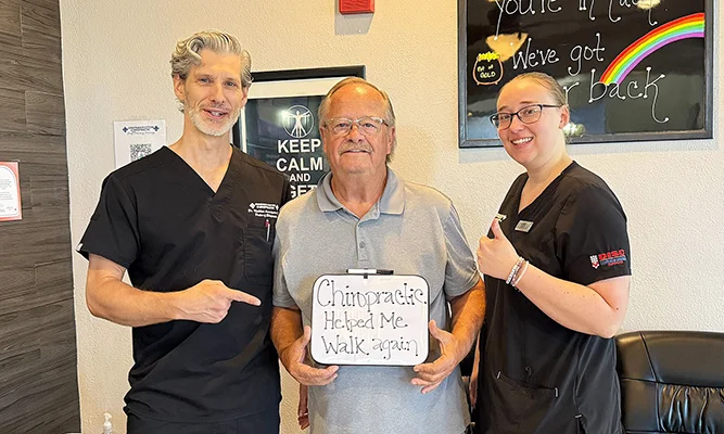 Patient with chiropractic staff holding a sign that reads, “Chiropractic helped me walk again!”