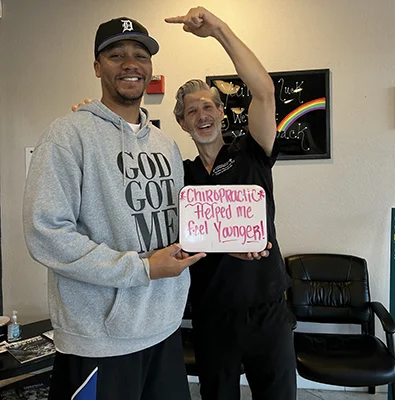 Patient and chiropractor holding a sign that reads, “Chiropractic helped me feel younger!”